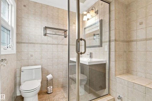 Tile-clad bathroom featuring a glass-enclosed shower, built-in shower bench, single vanity with integrated sink, and a casement window - 14103 60 Avenue Nw, Edmonton, AB 