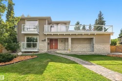 Stucco exterior with stone veneer accents, double entry doors, multiple balconies with glass railings, and a paver walkway - 
