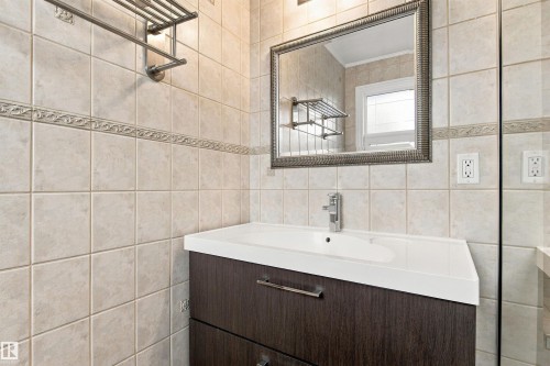 Bathroom featuring a wood-finish vanity with an integrated sink, polished chrome faucet, and a decorative framed mirror - 14103 60 Avenue Nw, Edmonton, AB 