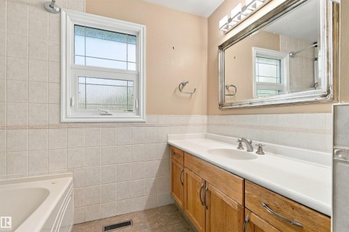 Bathroom featuring a window with privacy glass, a built-in bathtub, a vanity with an integrated sink, a large framed mirror, and a three-light fixture - 14103 60 Avenue Nw, Edmonton, AB 