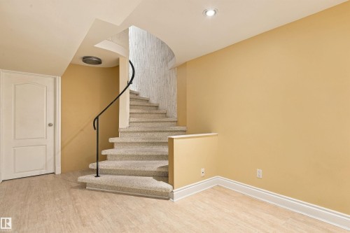 Curved staircase with a wrought iron railing, recessed ceiling lighting, wood-finish flooring, and a paneled door - 14103 60 Avenue Nw, Edmonton, AB 