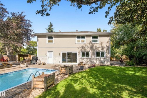 Two-story exterior with stucco and stone accents, featuring an in-ground swimming pool, brick paver patio, and sliding glass doors - 14103 60 Avenue Nw, Edmonton, AB 