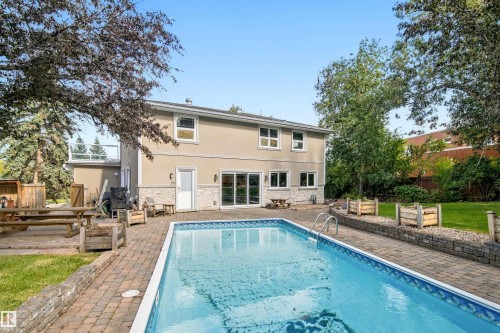 Stucco exterior with stone accenting, patio with brick paver flooring, in-ground swimming pool, and a second-level balcony with glass railing - 14103 60 Avenue Nw, Edmonton, AB 