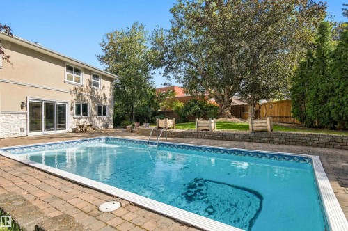 Outdoor swimming pool with brick paver surround, stucco exterior, stone accent cladding, and large sliding glass doors - 14103 60 Avenue Nw, Edmonton, AB 