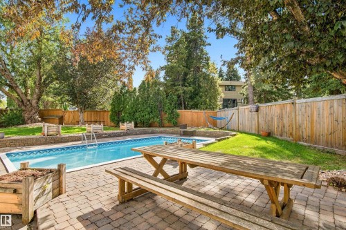 Expansive backyard featuring a swimming pool with a metal ladder, paver patio, wood fencing, and mature trees - 14103 60 Avenue Nw, Edmonton, AB 