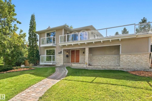 Stucco exterior with stone accenting, dual wooden entry doors, upper-level balcony with glass railing, and a paver walkway - 14103 60 Avenue Nw, Edmonton, AB 