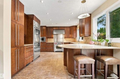 Gourmet kitchen with extensive wood cabinetry, stainless steel appliances, tile flooring, and a stone countertop island - 14103 60 Avenue Nw, Edmonton, AB 