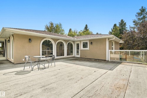 Expansive outdoor patio with concrete surfacing, multiple arched windows, stucco exterior, and a glass-paneled railing - 14103 60 Avenue Nw, Edmonton, AB 