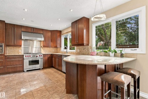 Gourmet kitchen featuring wood cabinetry, stainless steel appliances, tile backsplash, stone countertops, and a breakfast bar - 14103 60 Avenue Nw, Edmonton, AB 