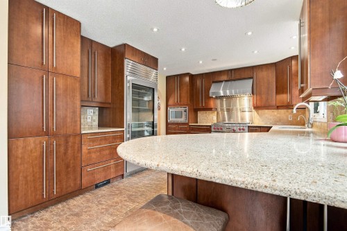 Rich wood cabinetry with linear hardware, integrated stainless steel refrigerator, stone countertops, stainless steel range with overhead hood, and recessed lighting - 14103 60 Avenue Nw, Edmonton, AB 