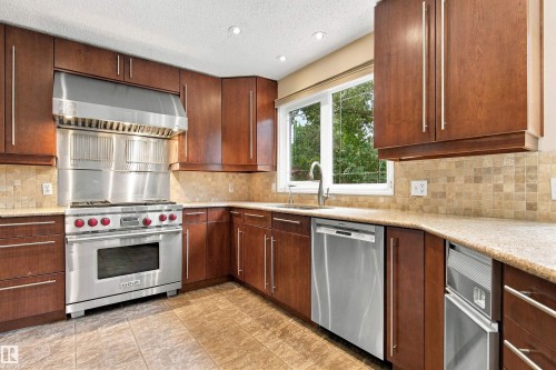 Kitchen featuring wood cabinetry, stainless steel appliances, mosaic tile backsplash, composite countertops, and tile flooring - 14103 60 Avenue Nw, Edmonton, AB 