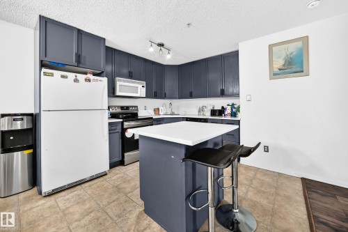 Kitchen featuring dark cabinetry, white countertops, built-in microwave, and tile flooring - #133 16311 95 St Nw, Edmonton, AB 