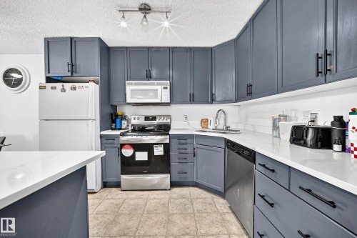 Kitchen featuring painted cabinetry, light-toned countertops, a stainless steel range, and a built-in microwave - #133 16311 95 St Nw, Edmonton, AB 