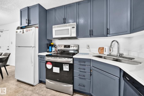 Kitchen featuring shaker-style cabinetry, stainless steel appliances, a corner sink, and light-toned countertops - #133 16311 95 St Nw, Edmonton, AB 