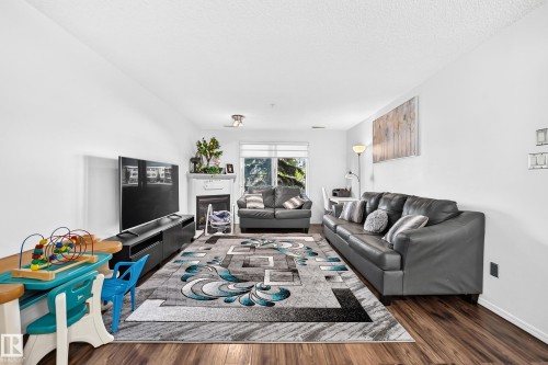 Wood-finish flooring throughout, white walls, and a recessed fireplace with a white mantel and hearth - #133 16311 95 St Nw, Edmonton, AB 