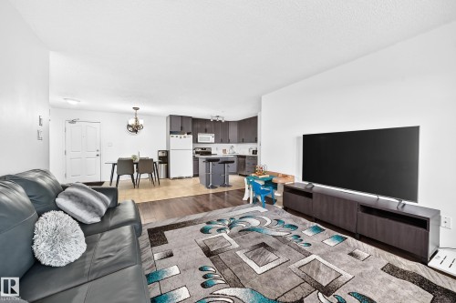 Open-concept living area featuring wood-finish flooring, dark wood-finish cabinetry, and stainless steel appliances - #133 16311 95 St Nw, Edmonton, AB 