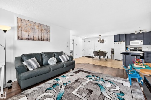 Open-concept living area with dark wood-finish flooring, white walls, and a kitchen featuring dark cabinetry, stainless steel appliances, and white countertops - #133 16311 95 St Nw, Edmonton, AB 