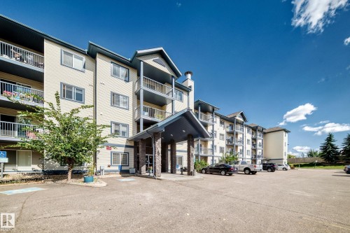 Multi-story building featuring a stone-clad entrance, multiple private balconies, and a paved parking area - #133 16311 95 St Nw, Edmonton, AB 
