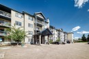 Multi-story building featuring a stone-clad entrance, multiple private balconies, and a paved parking area - #133 16311 95 St Nw, Edmonton, AB 