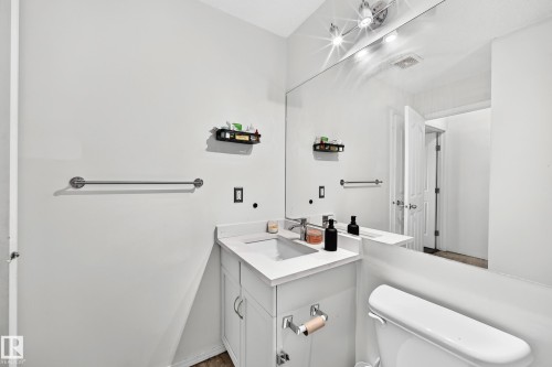 White vanity with a built-in sink, chrome faucet, wall-mounted mirror, and track lighting - #133 16311 95 St Nw, Edmonton, AB 