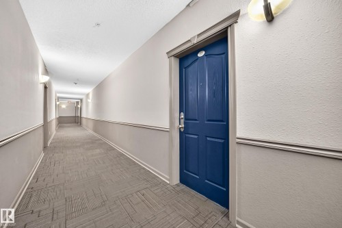 Hallway with patterned carpeting, wainscoting, and wall-mounted sconce lighting - #133 16311 95 St Nw, Edmonton, AB 