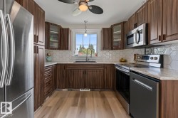 Kitchen featuring stainless steel appliances, wood-finish cabinetry, light-toned countertops, a white hexagonal tile backsplash, and light wood-finish flooring - 