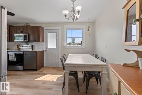 Kitchen and dining area featuring wood-finish flooring, dark wood cabinetry, stainless steel appliances, hexagonal tile backsplash, and a white paneled exit door - 1801 Forest Drive, Cold Lake, AB - Indoor