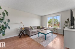 Living area featuring wood-finish flooring, light neutral wall tones, and a large window with white trim - 