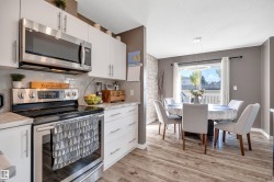 Modern kitchen with stainless steel appliances, white cabinetry, a subway tile backsplash, and wood-finish flooring extending into the dining area with a contemporary light fixture - 