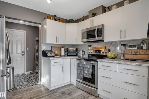 Modern kitchen featuring white cabinetry, stainless steel appliances, marble-look countertops, and wood-finish flooring - #13 6608 158 Av Nw, Edmonton, AB 