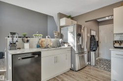 Kitchen with wood-finish flooring, white cabinetry, integrated stainless steel appliances, a tile backsplash, and a double basin sink - 