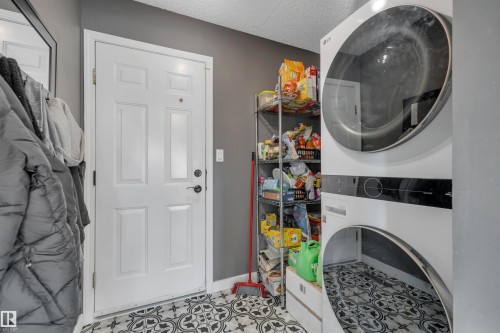 White paneled door with black hardware, patterned floor tiling, and a stacked white washer and dryer unit - #13 6608 158 Av Nw, Edmonton, AB 