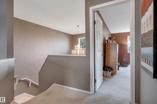 Carpeted flooring, white trim details, an interior doorway, and a chandelier with multiple light sources - #13 6608 158 Av Nw, Edmonton, AB 