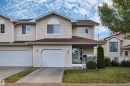 Cream-colored siding exterior, two attached single-car garages, white front porch railing, arched window accents, and a shingled roof - #13 6608 158 Av Nw, Edmonton, AB 