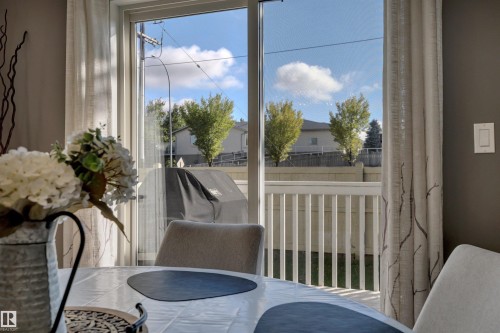 Sliding glass door opening to an outdoor deck with white railings, framed by neutral drapery and dark wall paint - #13 6608 158 Av Nw, Edmonton, AB 