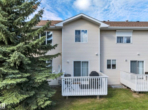 Multi-level structure featuring vinyl siding, multiple windows, and a built-in deck with railings - #13 6608 158 Av Nw, Edmonton, AB 