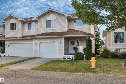 Multi-level facade with light-colored siding, double garage doors, and arched window - #13 6608 158 Av Nw, Edmonton, AB 