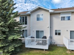 Rear exterior featuring light-colored siding, multiple windows, a private outdoor deck, and a sliding glass door - 