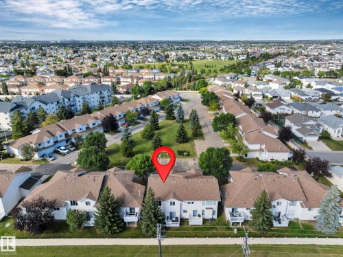 Townhouse complex featuring multiple units with white exteriors, brown shingle roofs, and private back patios - #13 6608 158 Av Nw, Edmonton, AB 