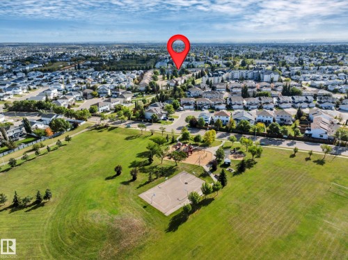 Expansive parkland featuring a large open field, playground, and paved sports court - #13 6608 158 Av Nw, Edmonton, AB 