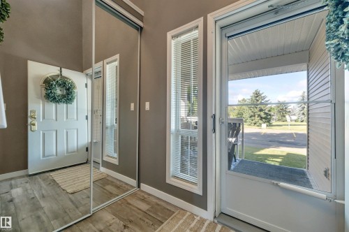Wood-finish flooring with a multi-paneled entry door, full-length mirrored closet doors, and side-light window with blinds - #13 6608 158 Av Nw, Edmonton, AB 