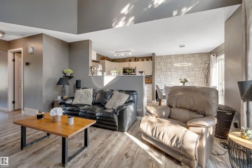 Living area with wood-finish flooring, two-tone painted walls, and a partial wall separating the kitchen - #13 6608 158 Av Nw, Edmonton, AB 