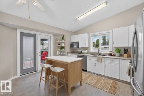 Wood-finish flooring with white cabinetry, a built-in microwave, and a stainless steel refrigerator - 365 Hollick-Kenyon Road Nw, Edmonton, AB 