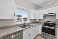 White cabinetry, dual basin stainless steel sink, stainless steel dishwasher, stainless steel range, and a coordinating range hood - 