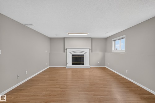 Expansive room featuring wood-finish flooring, a decorative fireplace with a white mantel, and a multi-pane window - 365 Hollick-Kenyon Road Nw, Edmonton, AB 