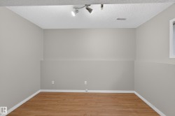 Wood-finish flooring, neutral wall paint, textured ceiling, track lighting, and a window with white trim - 