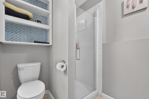 White toilet with a built-in shelving unit, patterned backing, and a shower with a glass enclosure - 365 Hollick-Kenyon Road Nw, Edmonton, AB 