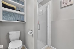 White toilet with a built-in shelving unit, patterned backing, and a shower with a glass enclosure - 