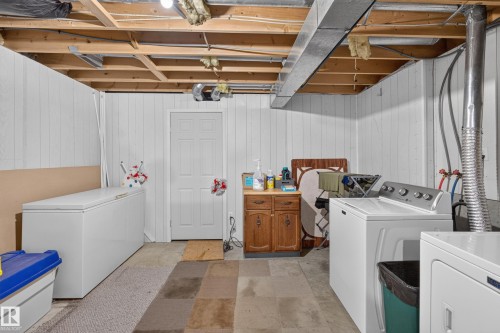 Unfinished basement utility space with exposed ceiling joists and ductwork, white paneled walls, and a built-in wood-finish cabinet with a countertop - 365 Hollick-Kenyon Road Nw, Edmonton, AB 