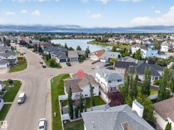 Aerial perspective of a residential neighborhood featuring a large body of water, multiple homes with varied architectural styles, and established landscaping - 